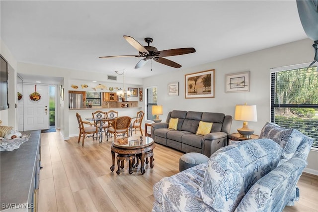 living area with visible vents, light wood-style flooring, and ceiling fan with notable chandelier