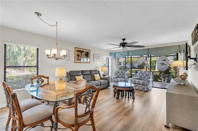 dining area with light wood finished floors, ceiling fan with notable chandelier, and a healthy amount of sunlight