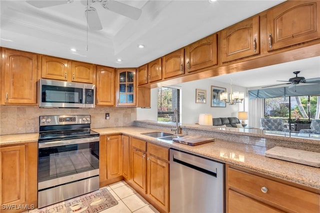 kitchen with appliances with stainless steel finishes, light stone counters, a tray ceiling, sink, and light tile patterned floors