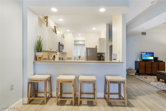 kitchen with kitchen peninsula, white cabinetry, light hardwood / wood-style flooring, appliances with stainless steel finishes, and a kitchen bar