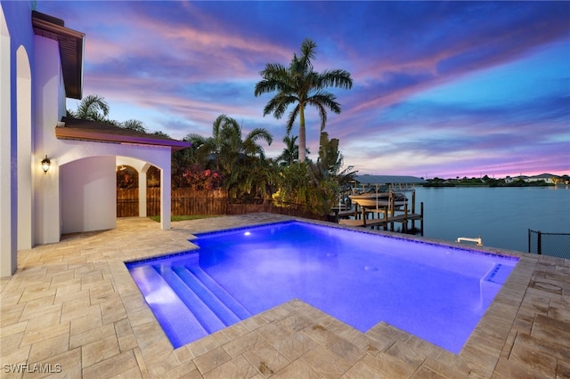 pool at dusk featuring a water view and a patio