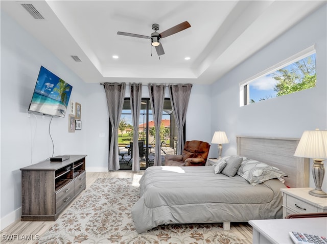 bedroom featuring a raised ceiling, light hardwood / wood-style flooring, access to exterior, and ceiling fan