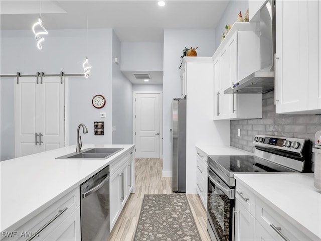 kitchen with appliances with stainless steel finishes, sink, a barn door, hanging light fixtures, and white cabinets