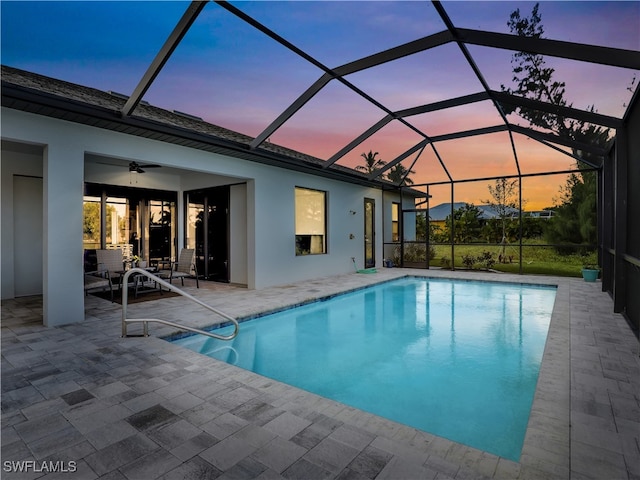 pool at dusk with a patio area, glass enclosure, and ceiling fan