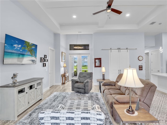 living room with ceiling fan, a raised ceiling, light wood-type flooring, and a barn door