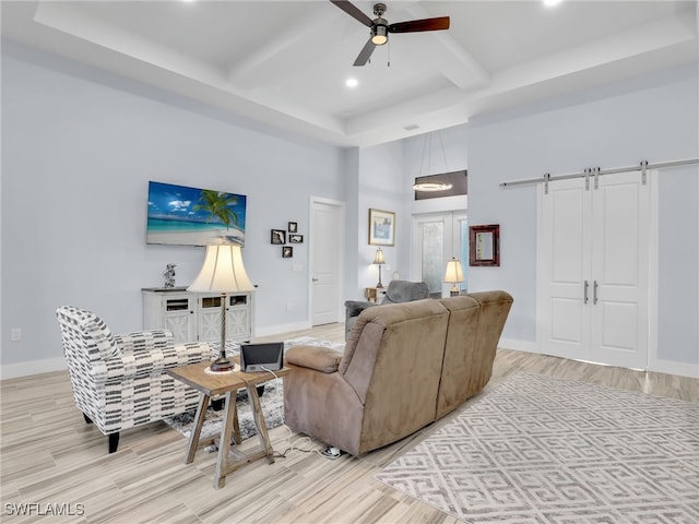 living room with ceiling fan, a barn door, beamed ceiling, a towering ceiling, and light hardwood / wood-style floors