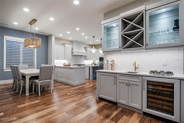 kitchen with wood-type flooring, wine cooler, pendant lighting, sink, and custom exhaust hood