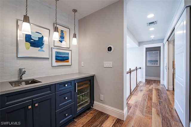 bar with wine cooler, decorative light fixtures, sink, dark wood-type flooring, and blue cabinets