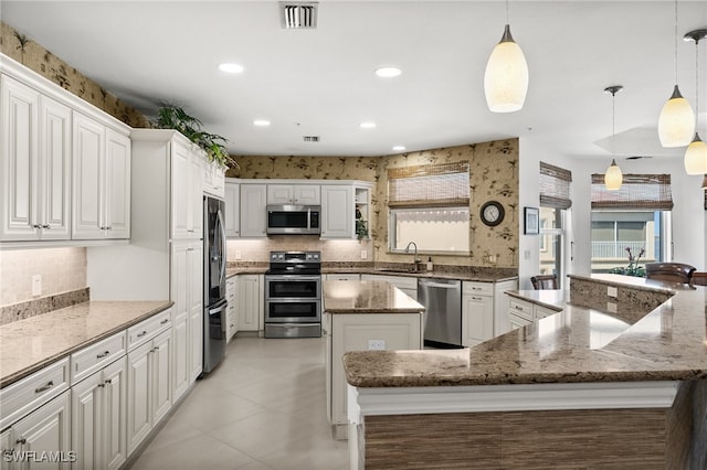 kitchen featuring white cabinetry, a center island, hanging light fixtures, light stone counters, and appliances with stainless steel finishes