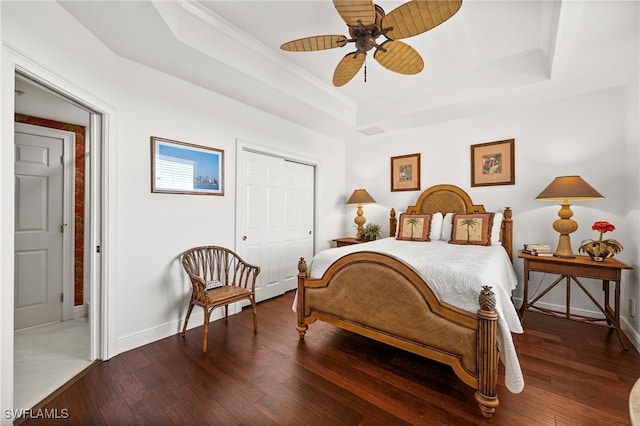 bedroom featuring a tray ceiling, dark hardwood / wood-style flooring, ceiling fan, and a closet