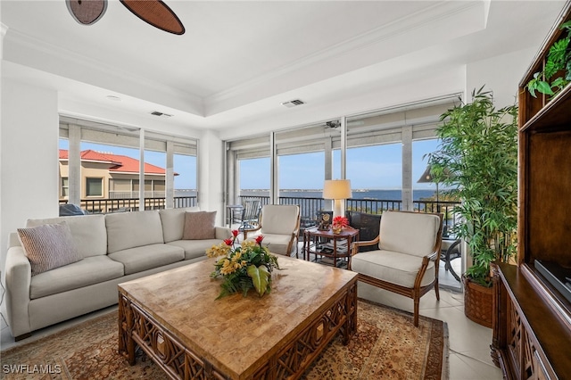 living room featuring ornamental molding, a tray ceiling, ceiling fan, a water view, and tile patterned flooring