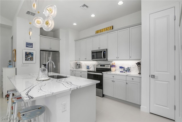 kitchen featuring decorative backsplash, light stone counters, stainless steel appliances, a center island with sink, and a breakfast bar area