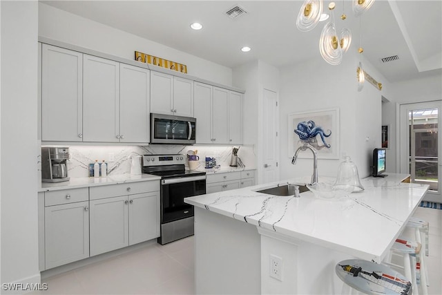 kitchen featuring a kitchen breakfast bar, sink, decorative backsplash, light stone counters, and stainless steel appliances