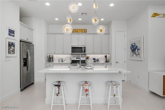 kitchen featuring a kitchen bar, backsplash, stainless steel appliances, hanging light fixtures, and an island with sink