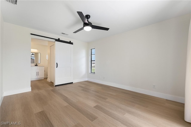 empty room with ceiling fan, light hardwood / wood-style flooring, and a barn door