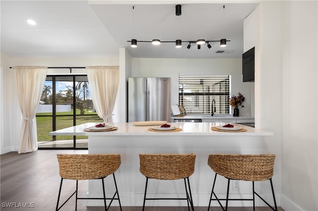 kitchen featuring dark wood-type flooring, sink, high end fridge, a kitchen bar, and track lighting