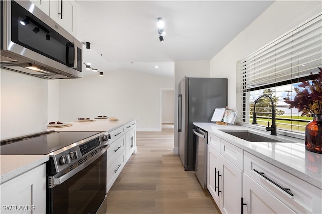 kitchen with sink, vaulted ceiling, white cabinetry, stainless steel appliances, and light hardwood / wood-style floors