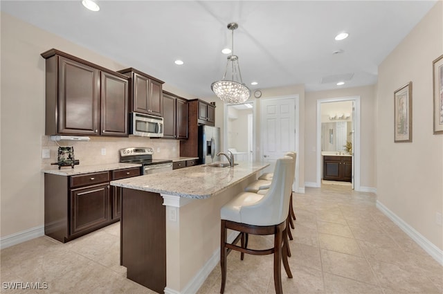 kitchen featuring tasteful backsplash, a center island with sink, hanging light fixtures, appliances with stainless steel finishes, and a kitchen bar