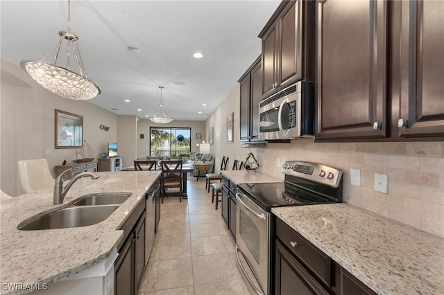 kitchen featuring sink, dark brown cabinets, decorative light fixtures, stainless steel appliances, and light stone countertops