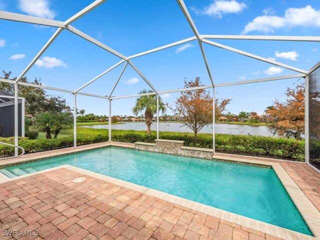 view of swimming pool with glass enclosure, a patio area, and a water view