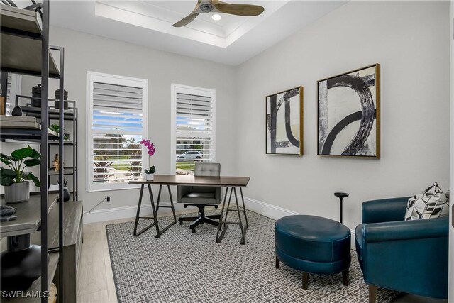 office with light hardwood / wood-style floors, a raised ceiling, and ceiling fan