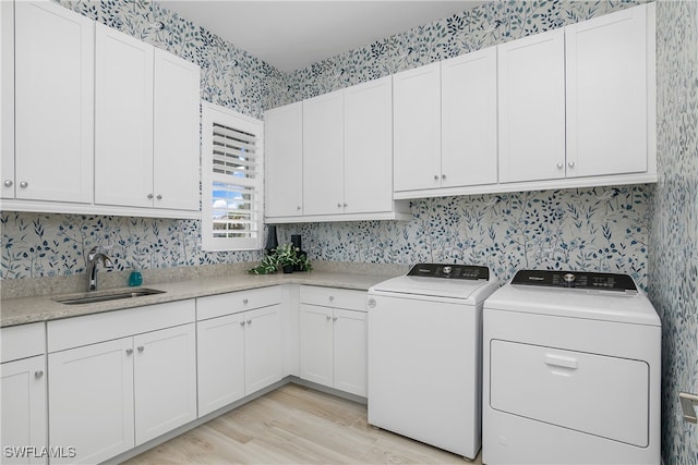 clothes washing area with cabinets, sink, light hardwood / wood-style flooring, and washing machine and clothes dryer