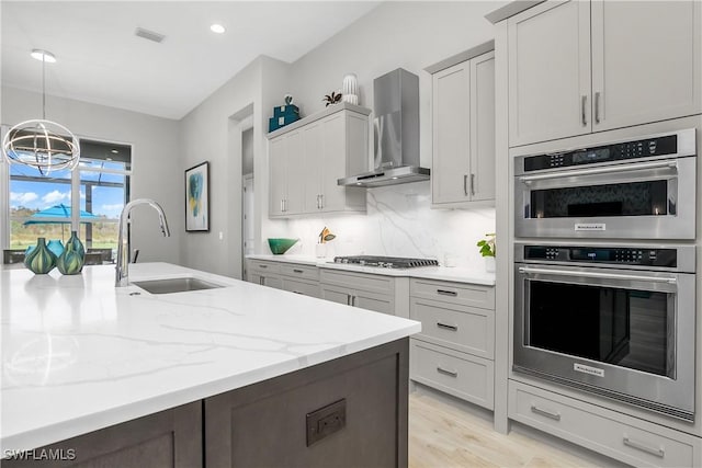 kitchen featuring appliances with stainless steel finishes, tasteful backsplash, sink, wall chimney range hood, and a chandelier