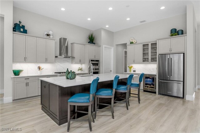 kitchen featuring a kitchen breakfast bar, wall chimney range hood, wine cooler, appliances with stainless steel finishes, and a large island