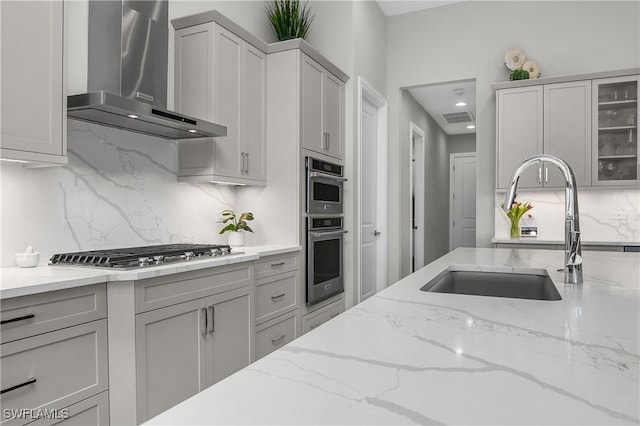 kitchen featuring appliances with stainless steel finishes, light stone counters, wall chimney exhaust hood, and sink