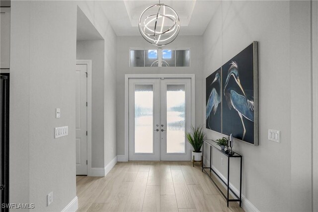 entryway with french doors, light hardwood / wood-style floors, and an inviting chandelier