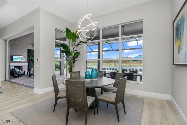 dining room with a large fireplace, light hardwood / wood-style flooring, a water view, and an inviting chandelier