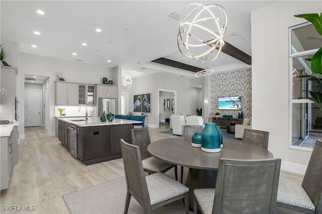 dining room featuring beam ceiling, sink, a chandelier, and light hardwood / wood-style floors