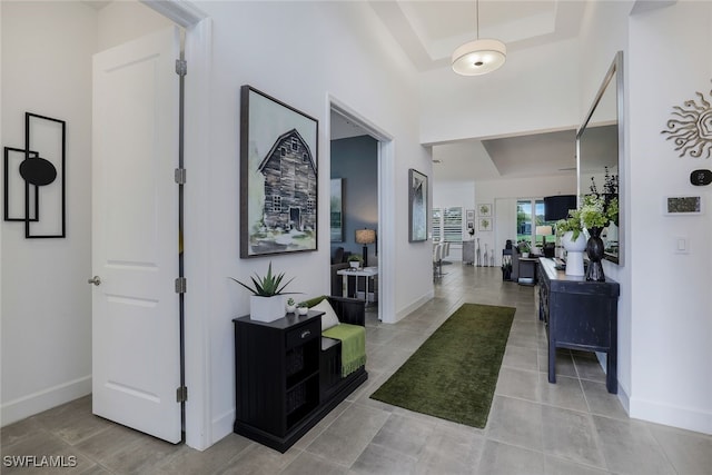 hall with a tray ceiling and tile patterned flooring