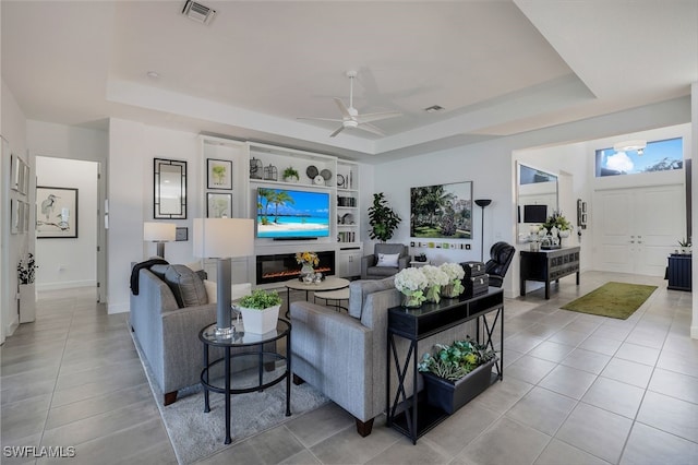 living room with ceiling fan, a raised ceiling, and light tile patterned flooring