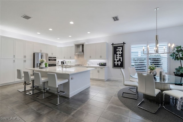 kitchen with wall chimney range hood, appliances with stainless steel finishes, a barn door, decorative light fixtures, and a notable chandelier