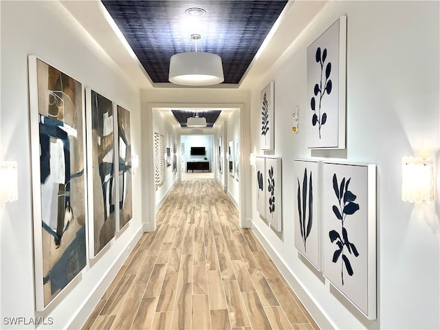 corridor featuring a tray ceiling and light hardwood / wood-style floors