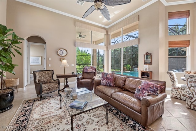 tiled living room with ceiling fan, a towering ceiling, and crown molding