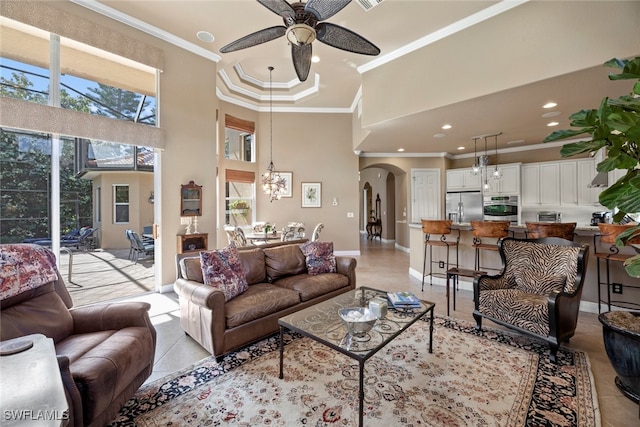 living room with ceiling fan with notable chandelier, a high ceiling, light tile patterned floors, and crown molding