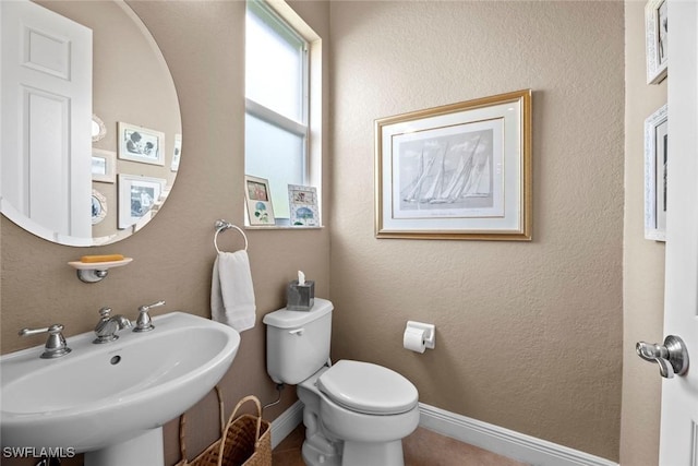 half bath with a textured wall, baseboards, a sink, and toilet