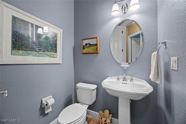 bathroom with a textured wall, toilet, and baseboards