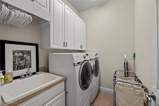 clothes washing area with baseboards, light tile patterned floors, cabinet space, washer and dryer, and a sink