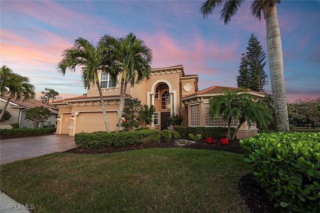 mediterranean / spanish home with decorative driveway, stucco siding, a lawn, a garage, and a tiled roof