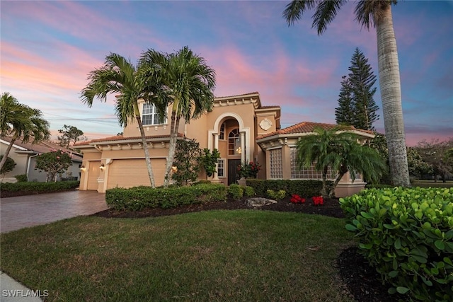 mediterranean / spanish-style house with a yard, driveway, a tiled roof, and stucco siding
