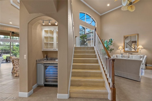 staircase with crown molding, bar, a ceiling fan, a healthy amount of sunlight, and beverage cooler