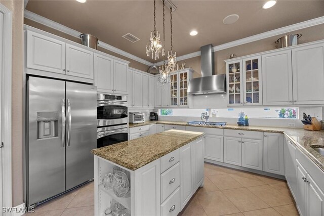 kitchen with a center island, stainless steel appliances, wall chimney exhaust hood, crown molding, and white cabinetry