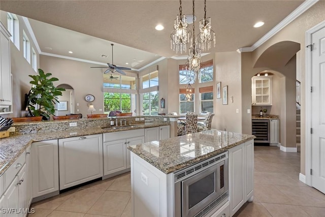 kitchen featuring stainless steel microwave, ornamental molding, recessed lighting, arched walkways, and ceiling fan with notable chandelier