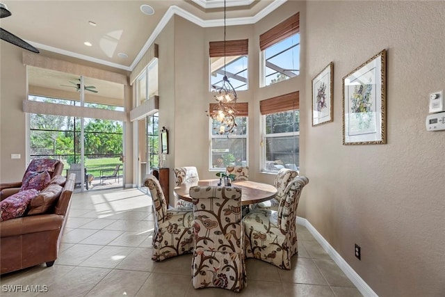 tiled dining area featuring a textured wall, ceiling fan with notable chandelier, a high ceiling, baseboards, and crown molding