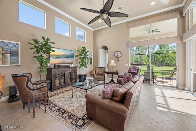 tiled living area with visible vents, arched walkways, ornamental molding, ceiling fan, and a towering ceiling