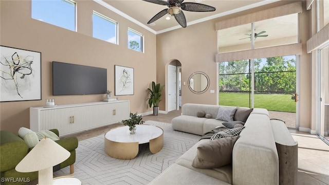 tiled living area with arched walkways, ornamental molding, a ceiling fan, a high ceiling, and baseboards