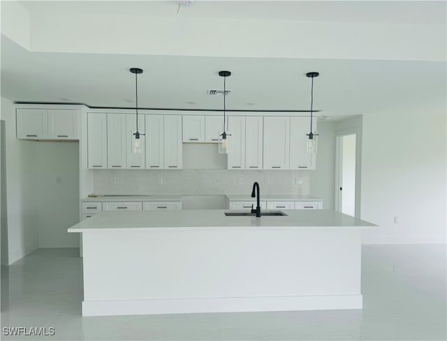 kitchen featuring pendant lighting, an island with sink, sink, and white cabinetry